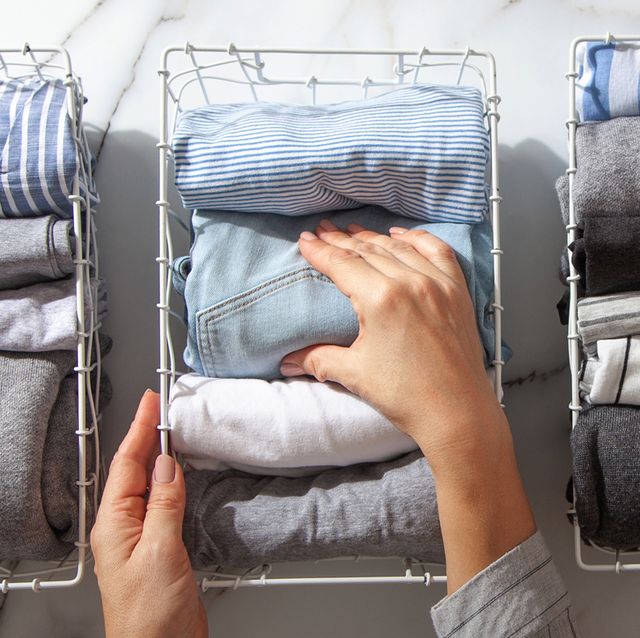 neatly folded clothes and pyjamas in the metal mesh organizer basket on white marble table marie kondo style of garments declutter and sorting concept housewife using konmari method of tidying up