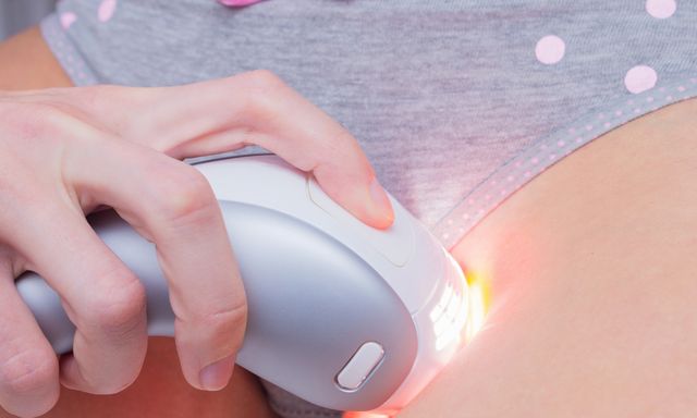 young woman with a ipl laser hair removal device shaving her bikini line removing unwanted hair and using the pulsed light epilator at home