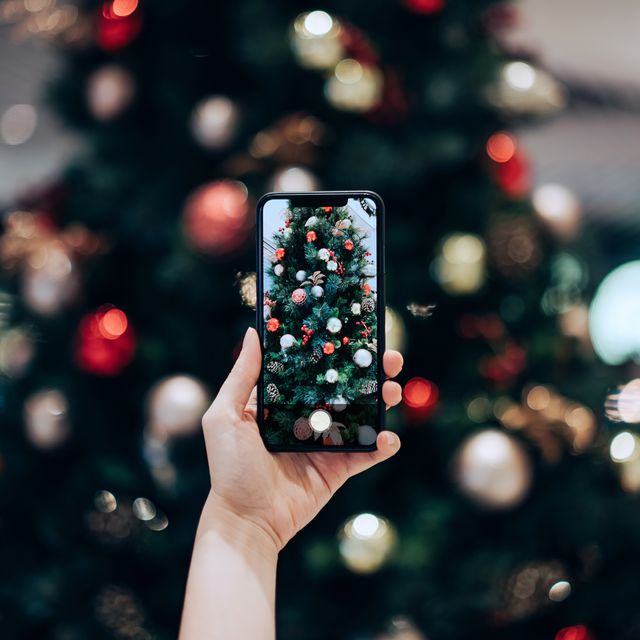 personal perspective of womans hand taking photo of a colourful christmas tree with smartphone in the festive christmas season