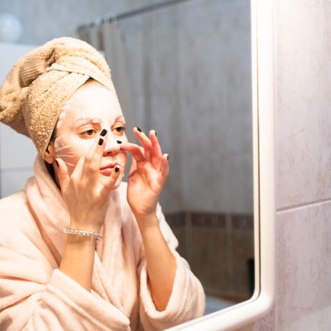 a beautiful young woman is applying a sheet mask in front of the mirror