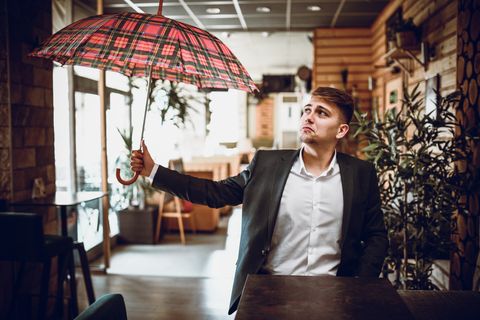 sad male sitting alone in coffee bar and opening umbrella