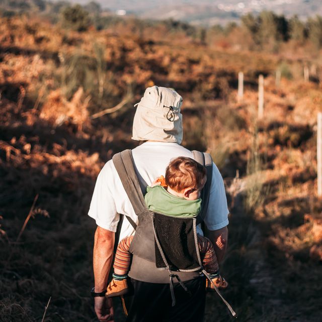 man carrying a child in a baby carrier on a path in the woods