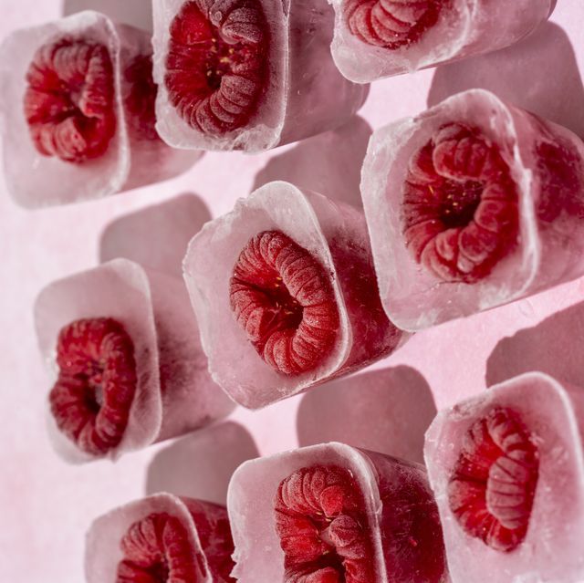 elevated view of some frozen raspberries inside ice cubes on a pink marble surface