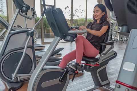 front view shot of an indonesian woman doing cardio exercise in an empty gym using a recumbent bike