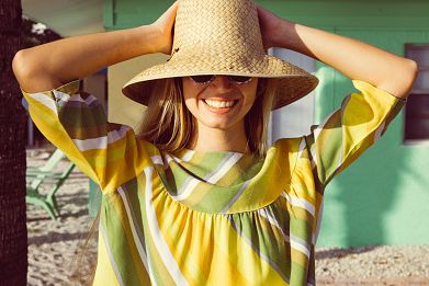 retro 1950s woman smiling on tropical beach vacation womans face is partially covered by her wide brim straw hat and sunglasses conceptual old fashion image for happiness, travel and traveling