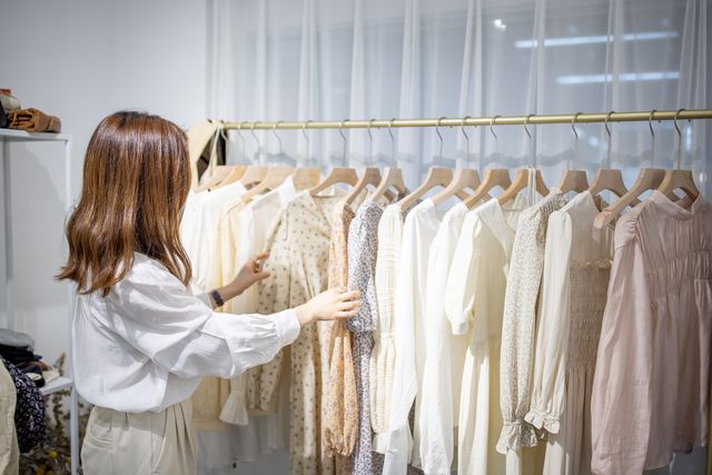 portrait of happy female asian entrepreneur working in her modern store with womenswear clothes, young chinese woman owner or consultant holding fashionable clothing while standing in brandy shop high quality photo