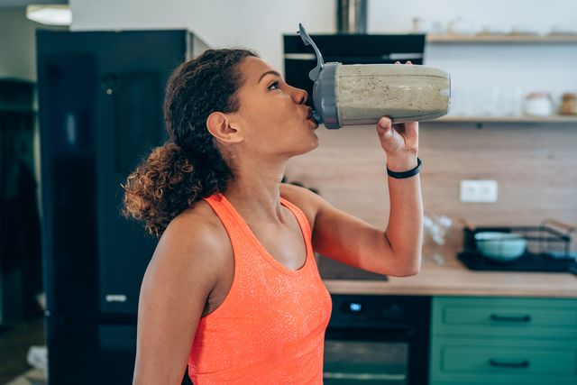 sportswoman drinking protein shake or smoothie after a home workout young female athlete drinking sports drink after exercising at home beautiful african american young woman resting after exercising training and drinking healthy smoothie