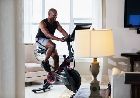a mid adult african american man in his 30s exercising at home in his living room, on an exercise bike he is an athlete with a muscular build