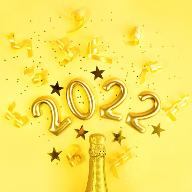 champagne bottle with golden glittering splashes in the shape of number 2022 and confetti on a trendy yellow background flat lay minimal party concept