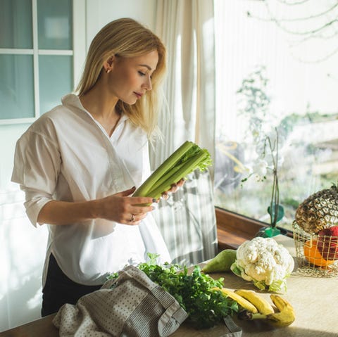 Beautiful woman unpacks a full fabric bag with fruits and vegetables on the kitchen. smiling young blonde woman organising fruits and vegetables from a reusable shopping bag on the kitchen table after grocery shopping zero waste concept vegan, vegetarian people nutritionist occupation