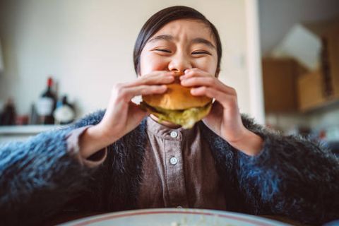 lovely cheerful girl enjoying her homemade burger at home