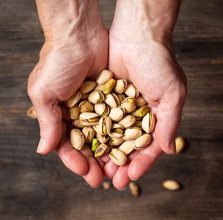 male hand holding roasted pistachio nuts above wooden table top view