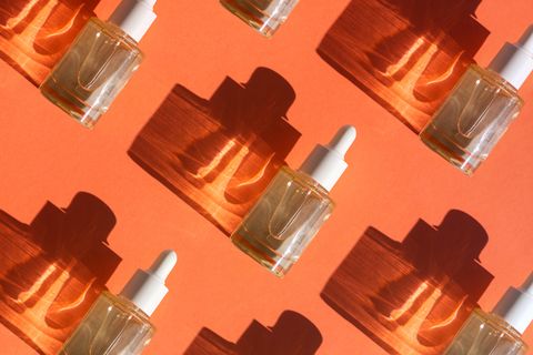 pattern made with glass bottle with cosmetic liquid on bright orange background with shadow and light reflections flat lay style and close up