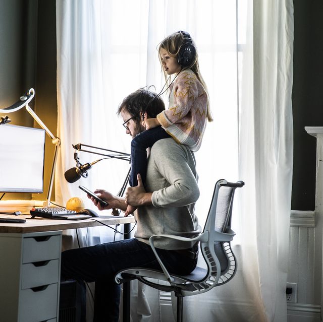 father working in home office with  young daughter on shoulders