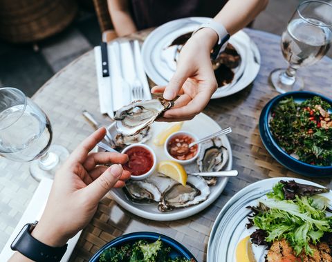 Vedere în unghi înalt a unei femei care îi dă bărbaților stridii proaspete peste masa în timpul prânzului, bucurându-se de o masă delicioasă într-un restaurant în aer liber, împărtășind și împreună, mâncând în stil de viață conceptul de mese în aer liber