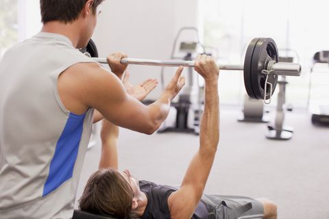 Man spotting friend lifting barbell in gymnasium