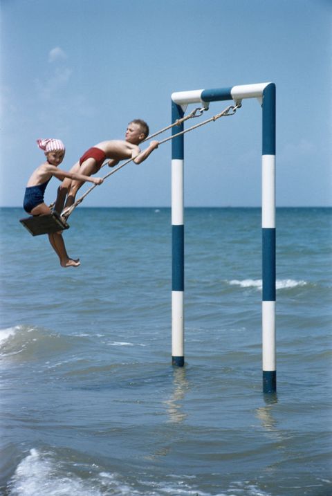 two children playing on a swing in the waters on the coast of rivabella, near rimini, on the adriatic riviera, italy, 1956 photo by slim aaronsgetty images
