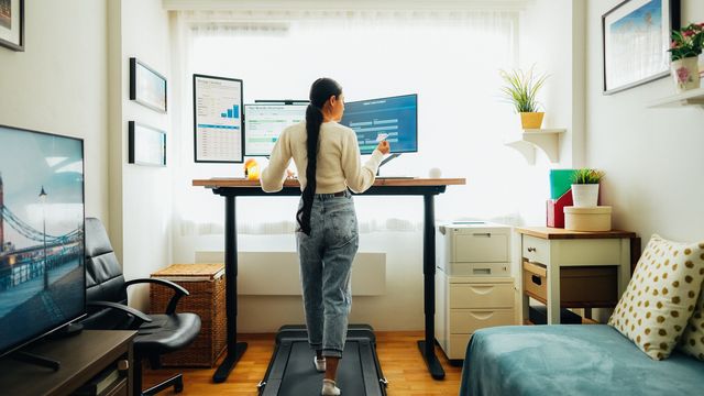 woman at home office making online payments while walking on under desk treadmill