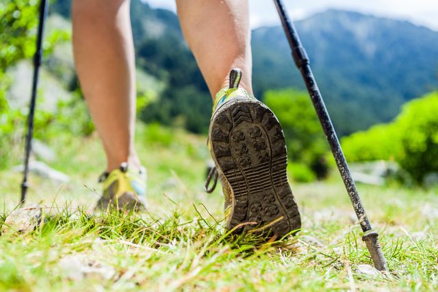 woman hiking in mountains, adventure and exercising nordic walking in sunny  summer nature outdoors legs and sport shoes walk on grass