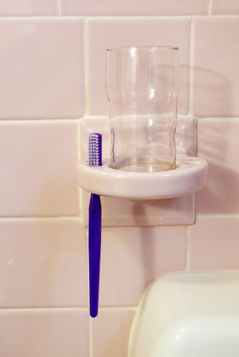 a single toothbrush with a glass in a holder on the tiled wall of a bathroom above the sink