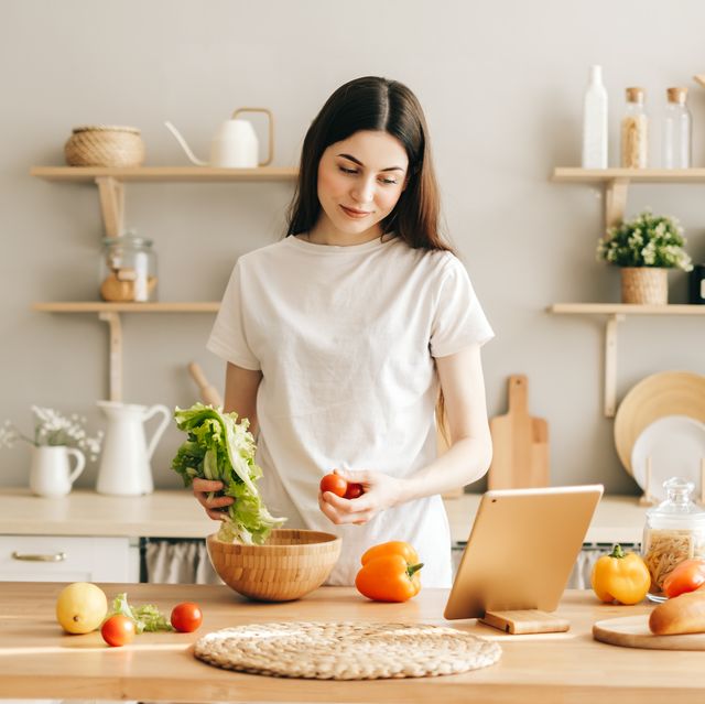 young caucasian woman use tablet computer in the modern kitchen, preparing salad, read recipe