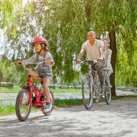 smiling family riding bicycle together on footpath by lake in public park smiling family riding bicycle together on footpath by lake in public park