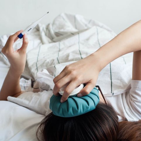 a young sick southeast asian woman with ice pack on her head is checking on her temperature using a digital thermometer while lying on her back