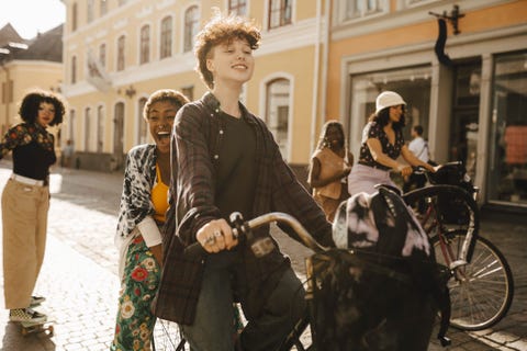 cheerful friends cycling and skateboarding on street in city