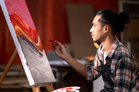 young asian male painting on canvas at studio