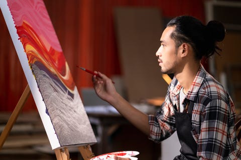 young asian male painting on canvas at studio