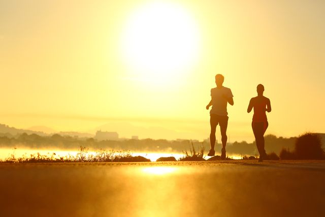 man and woman silhouettes running at sunrise in a coast road