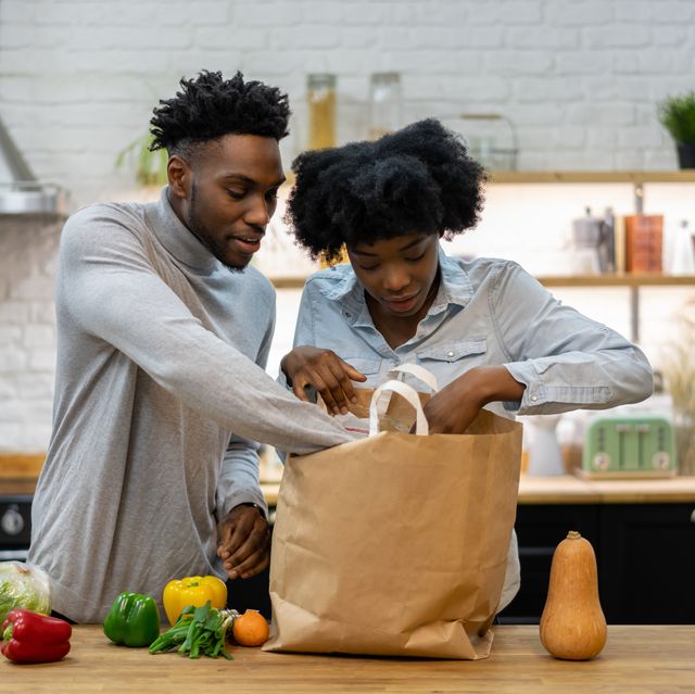 portrait of a happy african american couple at home unpacking the groceries from a shopping bagâ€“ lifestyle concepts