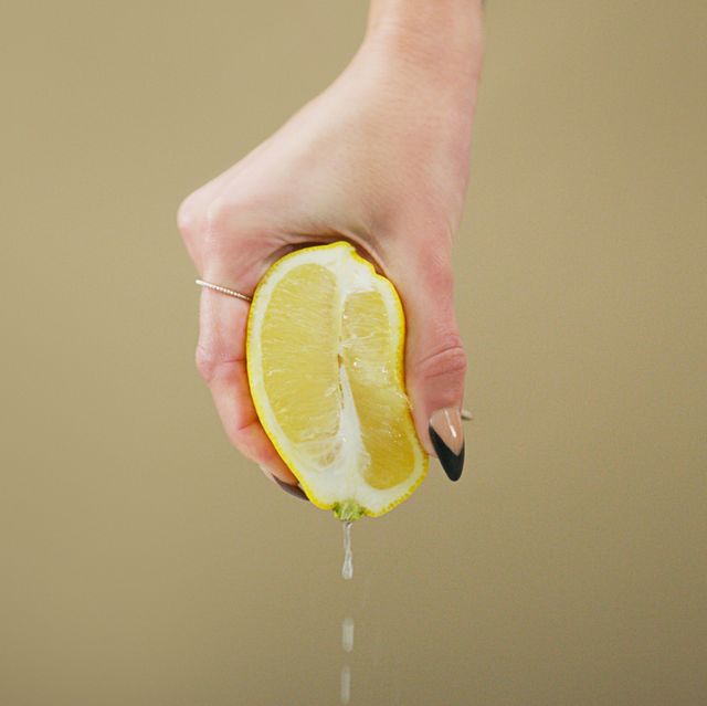 studio shot of an unrecognizable woman squeezing a lemon slice against a brown background
