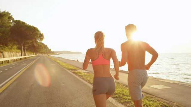 close up, sun flare unrecognizable young active couple runs down beautiful sunny ocean avenue sporty caucasian girlfriend and boyfriend on summer vacation jogging near the perfect golden lit seaside