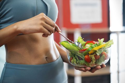 close up of a sport woman with her sexy belly, she holding a bowl of fresh healthy food