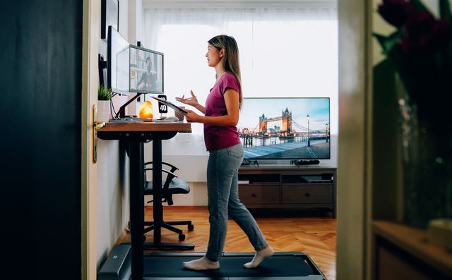 woman working from home at standing desk is walking on under desk treadmill