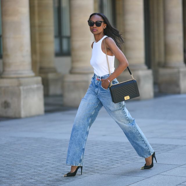 paris, france   july 04 emilie joseph wears black sunglasses, a white halter neck tank top, a black shiny grained leather boy shoulder bag from chanel, blue denim cut out high rise wide leg  boyfriend jeans pants from maison margiela, black satin with gold metallic pointed pumps heels shoes from saint laurent paris, during paris fashion week   haute couture fall winter 2022 2023, on july 04, 2022 in paris, france photo by edward berthelotgetty images