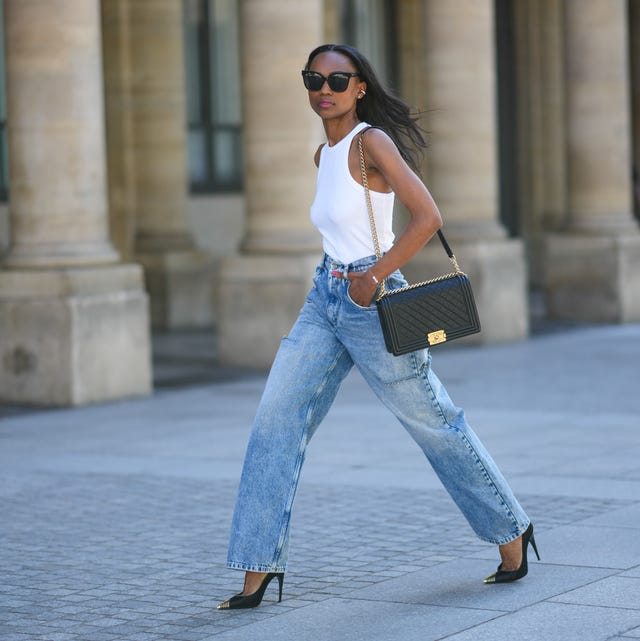 Street Style - Paris Fashion Week - Haute Couture Fall Winter 2022 2023 : Day One paris, france july 04 emilie joseph wears black sunglasses, a white halter neck tank top, a black shiny grained leather boy shoulder bag from chanel, blue denim cut out high rise wide leg boyfriend jeans pants from maison margiela, black satin with gold metallic pointed pumps heels shoes from saint laurent paris, during paris fashion week haute couture fall winter 2022 2023, on july 04, 2022 in paris, france photo by edward berthelotgetty images
