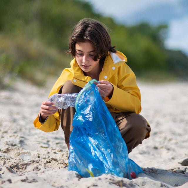 Preteen ecological girl cleaning beach from plastic waste. low angle view of adolescent girl in jacket picking up plastic garbage on sandy beach
