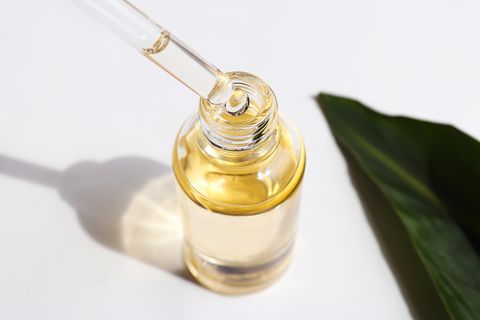 bottle of cosmetic essential oil and green leaf serum oil is dripping from dropper close up beauty and body care concept serum skin care product hard light