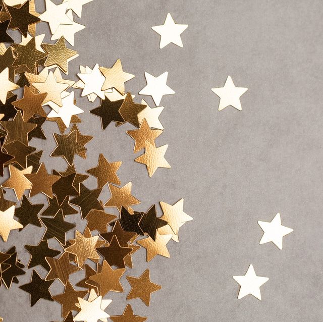 top view of shiny star shaped confetti placed in heap on side of gray background illuminating new year backdrop