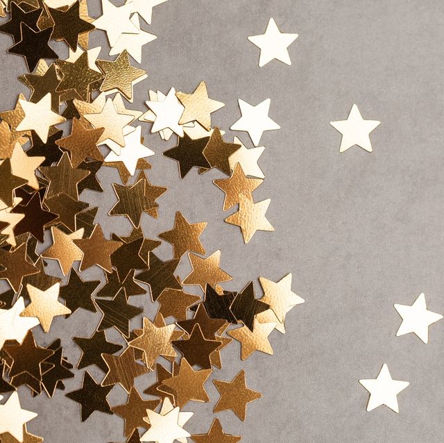 top view of shiny star shaped confetti placed in heap on side of gray background illuminating new year backdrop