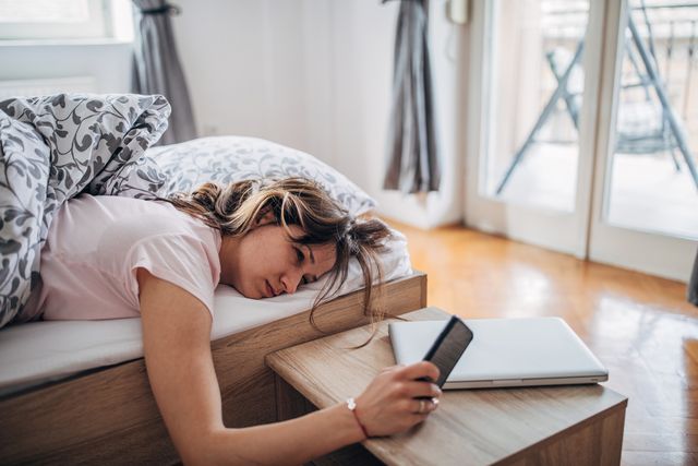 young woman is waking up and looking at her smart phone