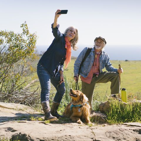 pasangan senior berfoto selfie dengan anjing saat mendaki di hari yang cerah