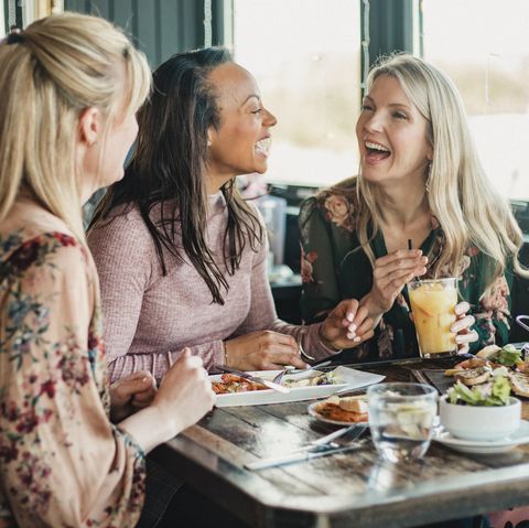 bidikan tampak depan dari tiga wanita paruh baya yang menikmati makan siang bersama di sebuah restoran