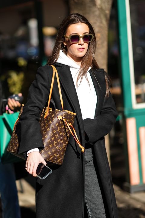 new york, new york   february 11 a guest wears sunglasses, a white hoodie sweater, a black long coat, a brown lv monogram print pattern neverfull shoulder bag from louis vuitton, gray denim jeans pants, outside herve leger, during new york fashion week, on february 11, 2022 in new york city photo by edward berthelotgetty images