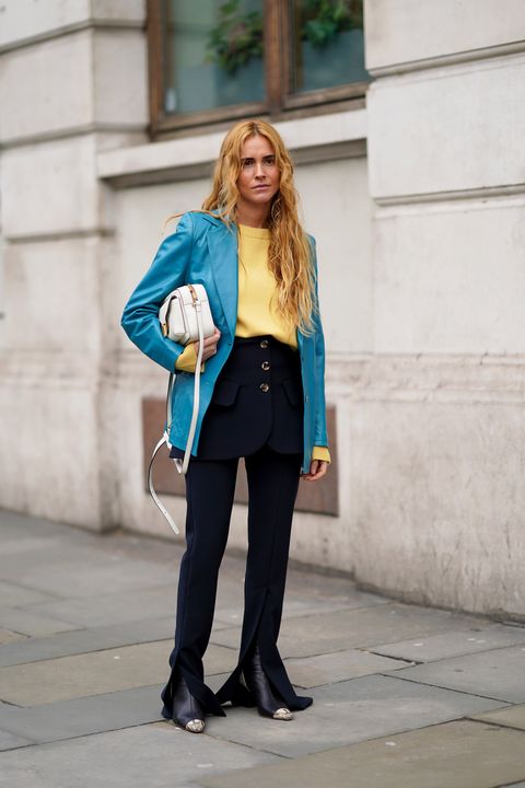 london, england   february 17 blanca miro wears a blue blazer jacket, a yellow pullover, a dark short skirt with buttons, dark flared pants, pointy boots, a white bag, during london fashion week february 2020 on february 17, 2020 in london, england photo by edward berthelotgetty images