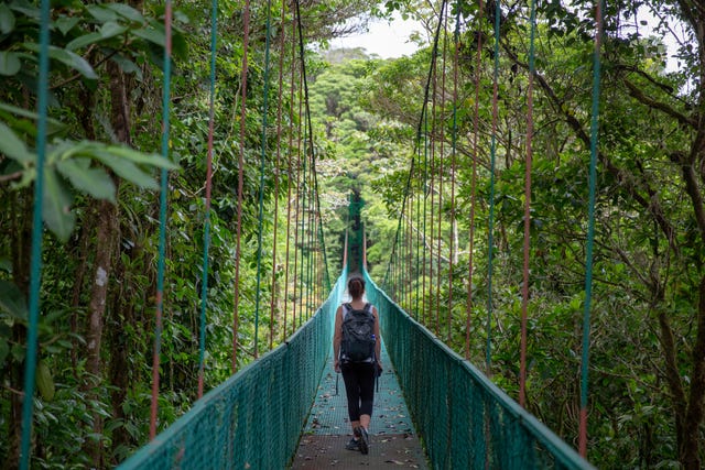 woman walking across hanging bridge with backpack on in monteverde, costa rica