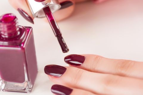 young beautiful girl with paint brush and bottle applying red wine manicure nails polish on finger on white desk manicure and girl fashion and beauty concept close up, selective focus