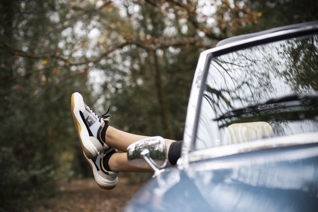 legs of carefree young woman in athletic shoes relaxing in convertible with feet out window in autumn park